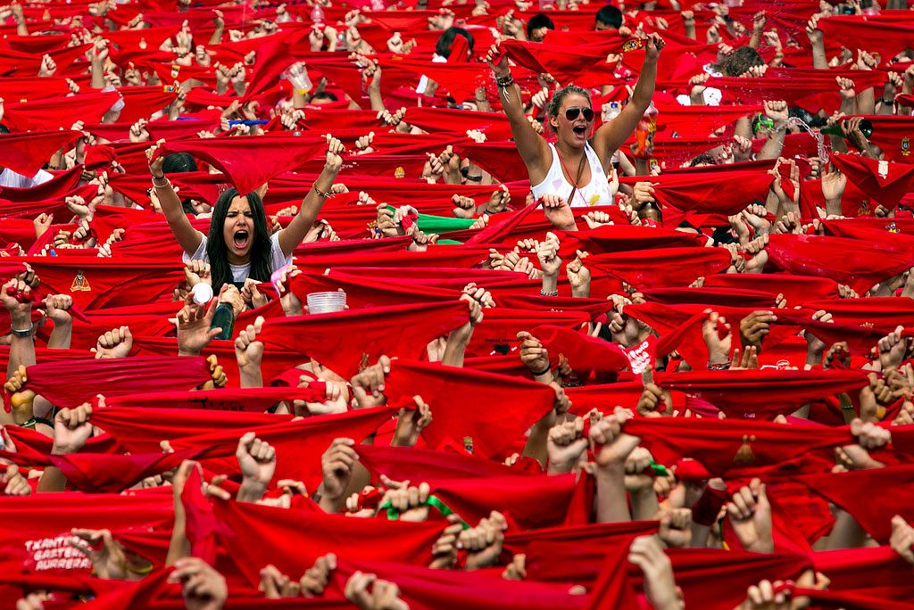Imagen del Chupinazo de Sanfermin obtenida por Carlos Mediavilla. Se ve al público de frente con los pañuelos rojos de cara y sobresalen dos chicas de blanco con los pañuelos al aire.